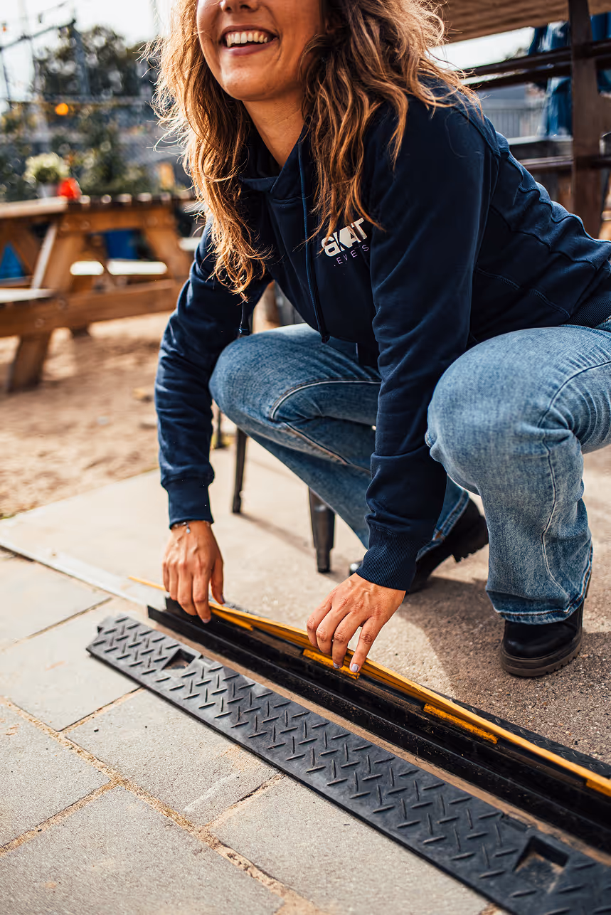 Vrouw hurkt buiten en legt een kabelbeschermer op de grond terwijl ze glimlacht.
