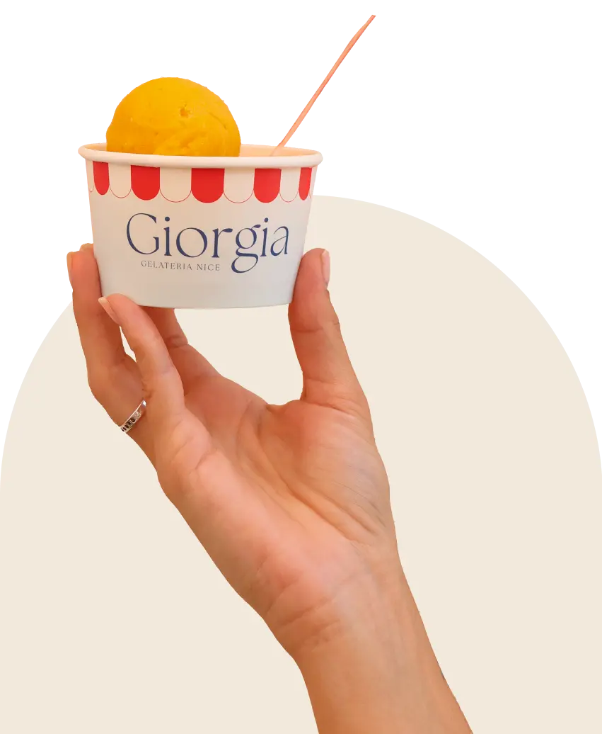 Une main qui tient un petit pot de glace Giorgia avec une boule de glace mangue à l’intérieur