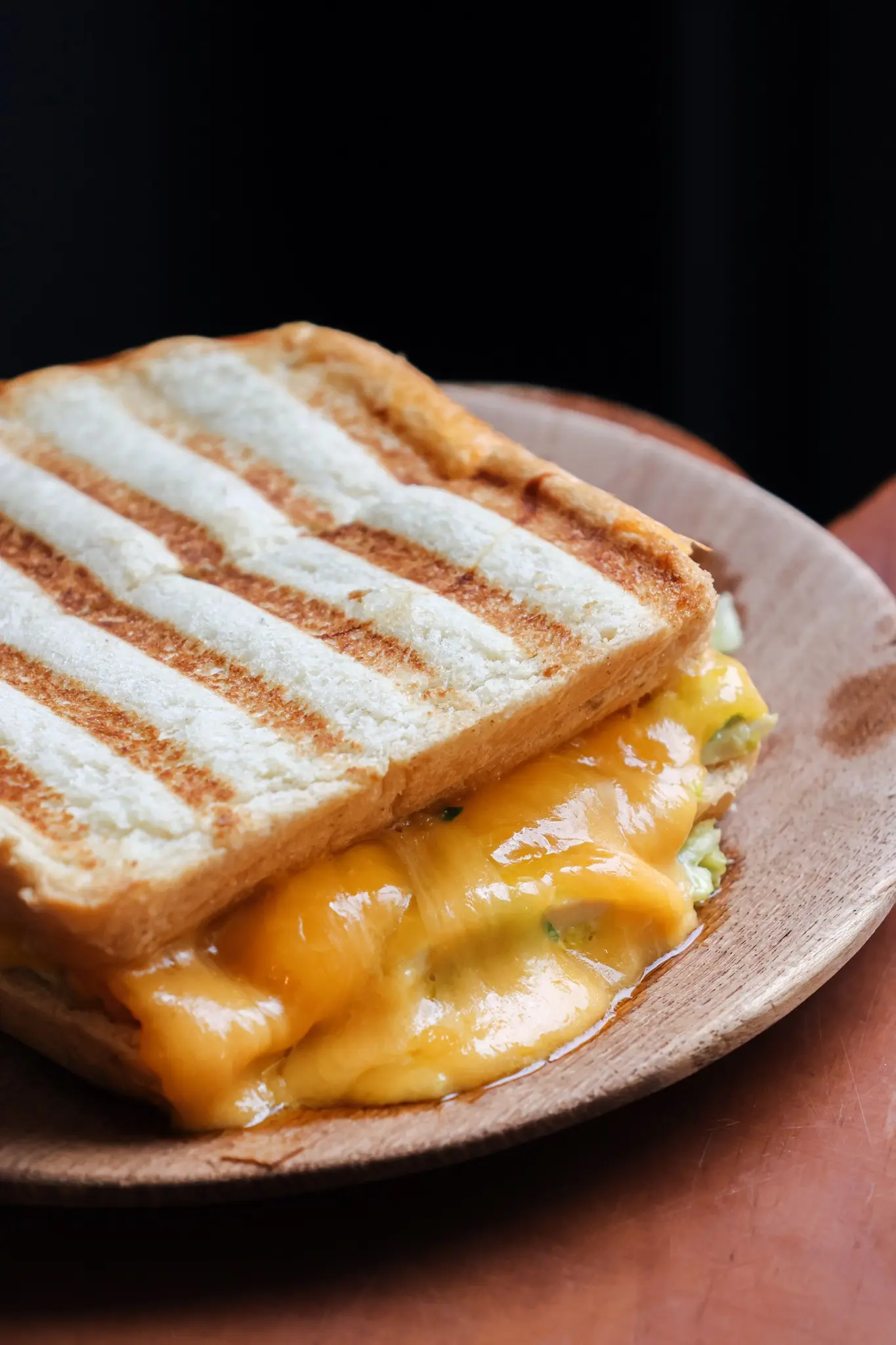 Notre sandwich club poulet toasté posé sur une assiette, avec du fromage fondant sortant des deux tranches