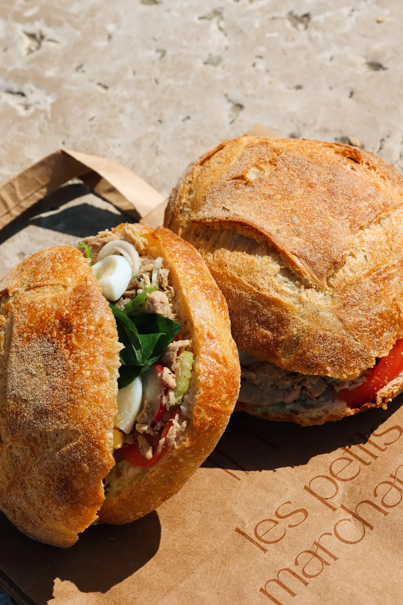 Deux pan bagnats posés l’un sur l’autre sur un sac kraft les petits marchands, au soleil