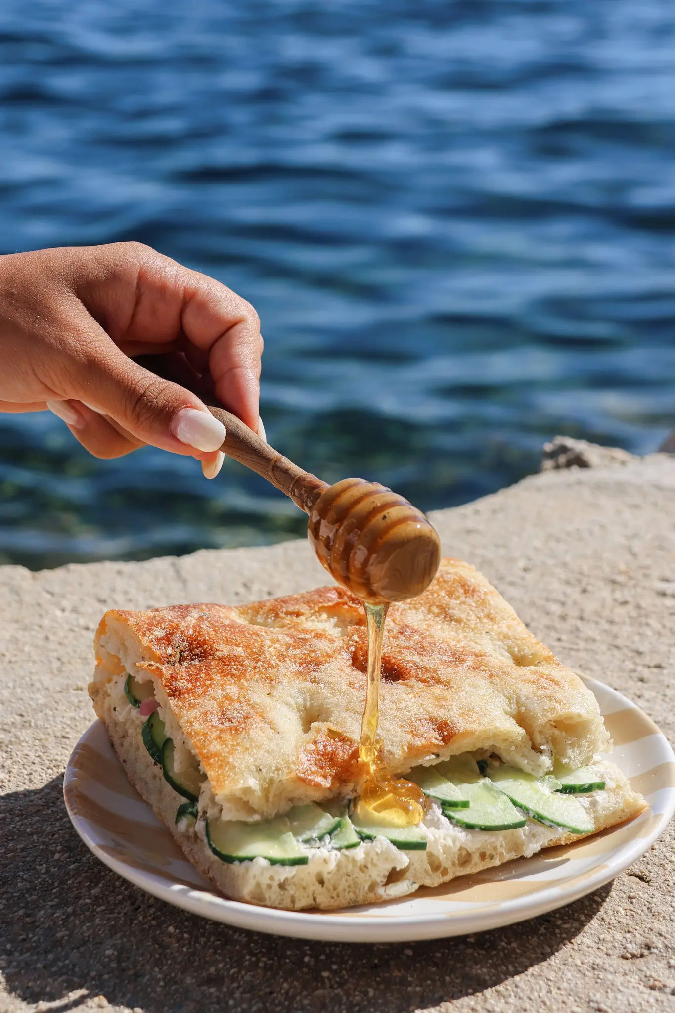 Une main faisant couler du miel sur une focaccia honey fêta les petits marchands face à la mer