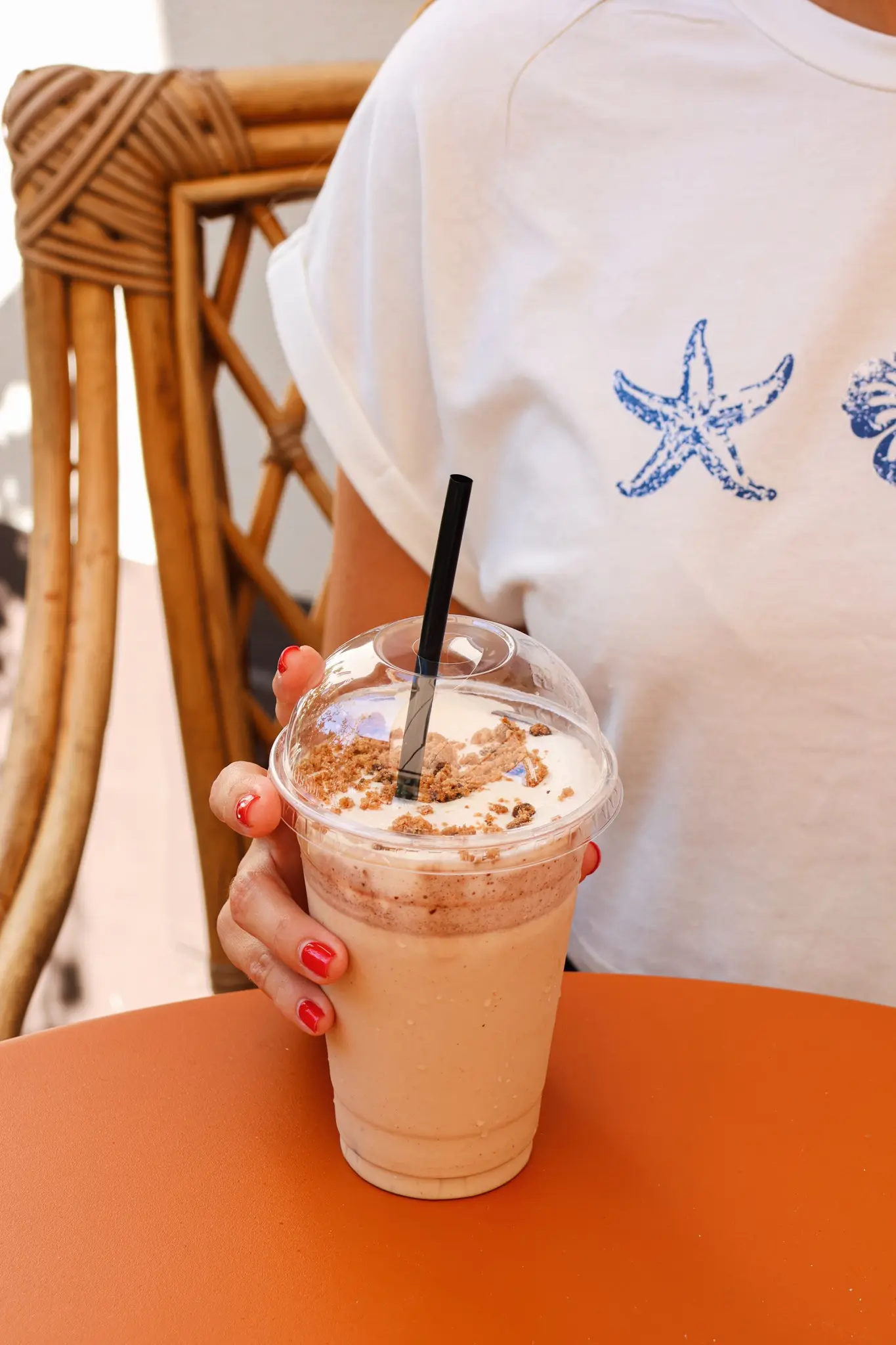 Une main qui tient un gobelet transparent avec la boisson du mois d’août : le freddo cookie cream, un café frappé au cookie