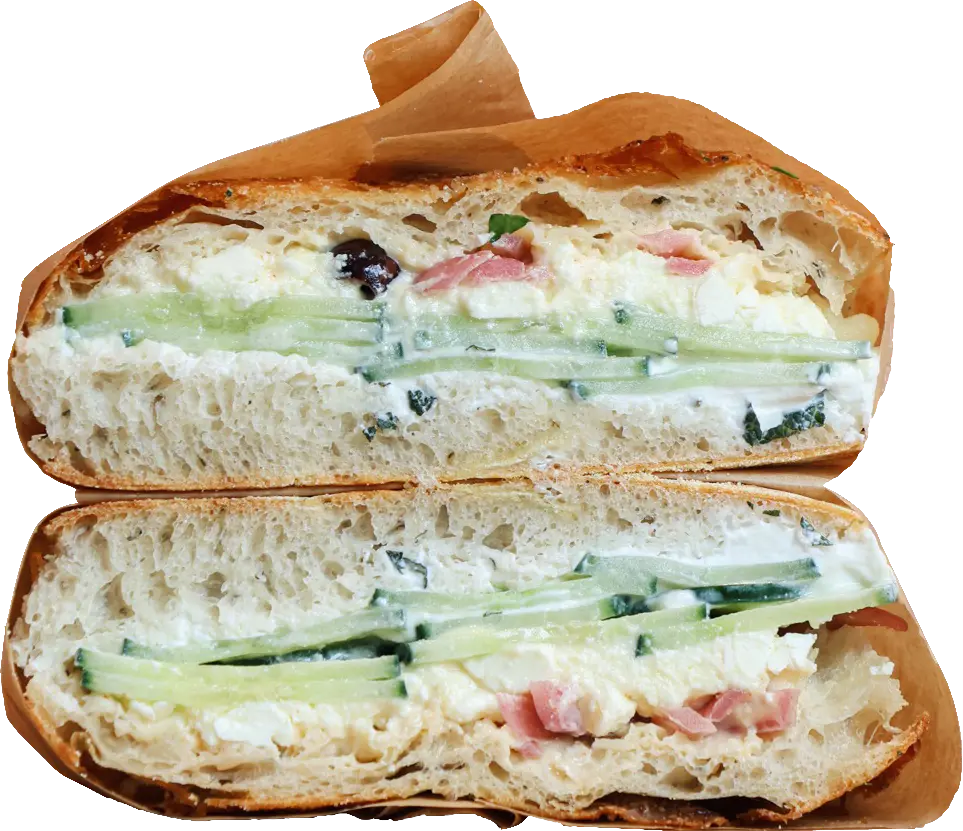 Une focaccia honey feta confectionnée par notre équipe snacking, coupée en deux et prise de face. On y voit les différentes couches de concombre, feta, et oignon pickles