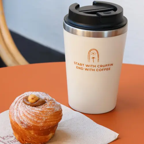 Mug à emporter, posé sur une table avec un cruffin à côté