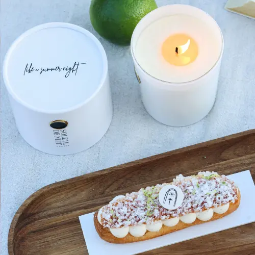  ⁠Photo prise de haut avec la tropézienne fleur d’oranger vanille citron vert, à côté la bougie allumée avec son packaging avec noté « like a summer night », à côté d’un citron vert