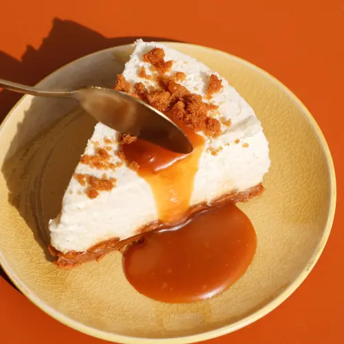 Part de cheesecake speculoos avec caramel coulant sur une assiette et une cuillère sur le dessus 