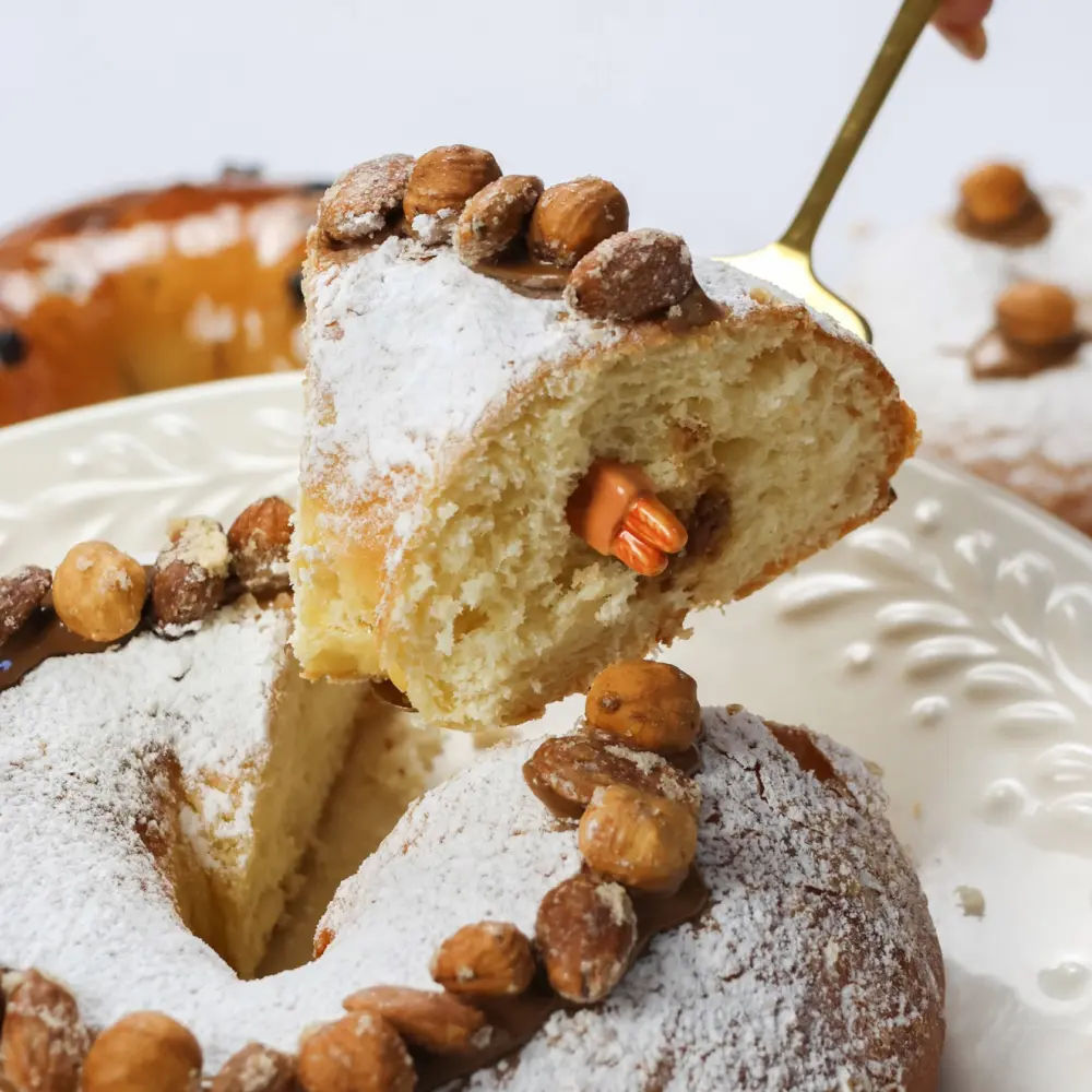 Zoom sur une part de brioche des Rois “Praliné noisette et amandes torréfiées” avec la fève qui dépasse de la part