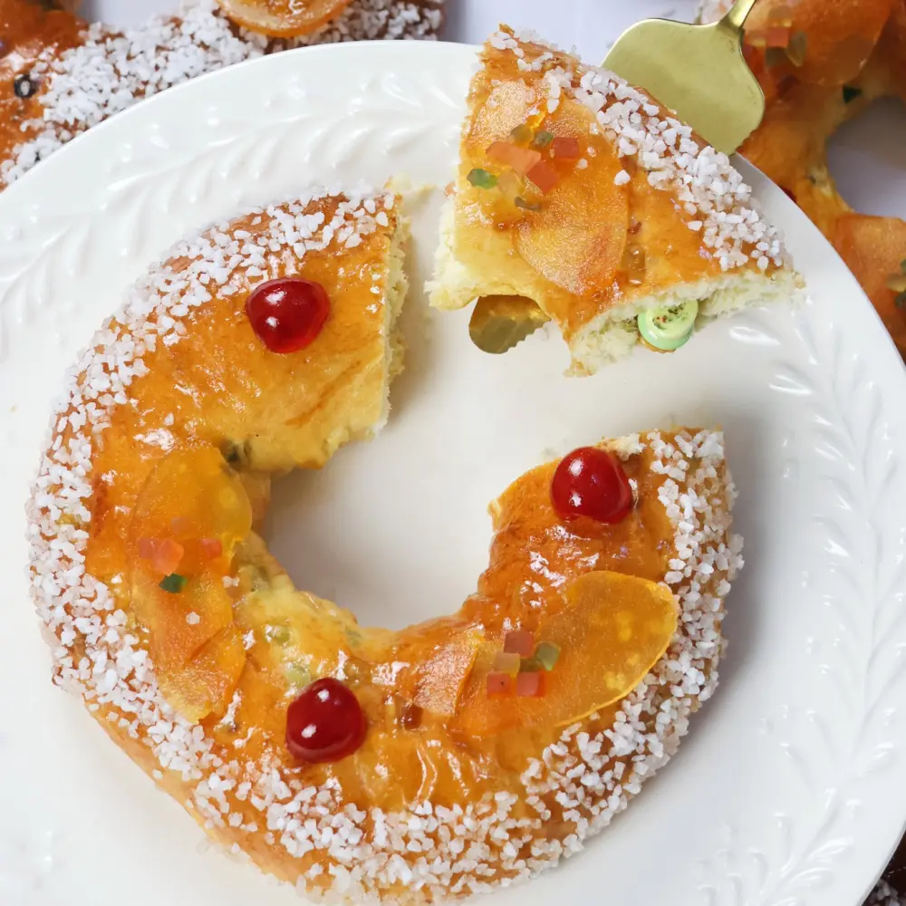 Une main prend une part de brioche “fruits confits” avec des morceaux de fruits confits et du sucre grain au-dessus