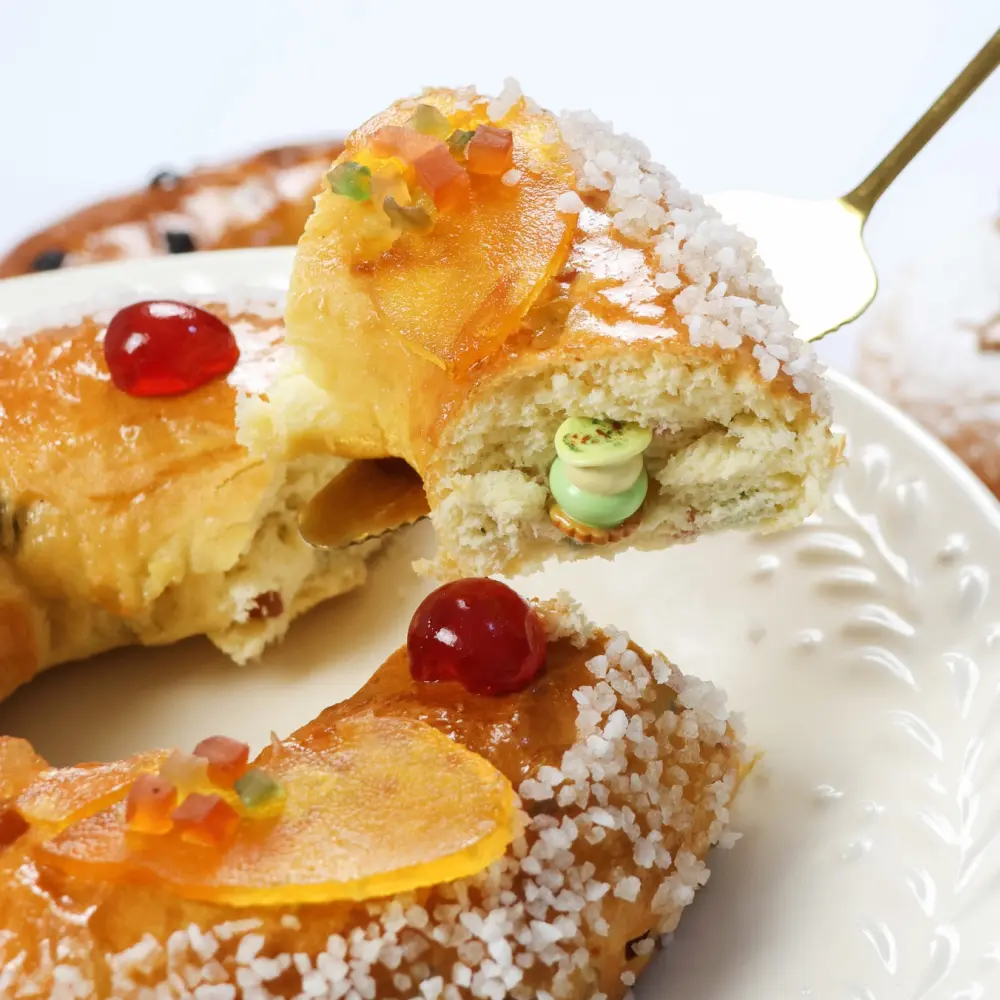 Zoom dur une part de brioche des Rois “fruits confits” , avec la fève qui sort sur le côté de la part