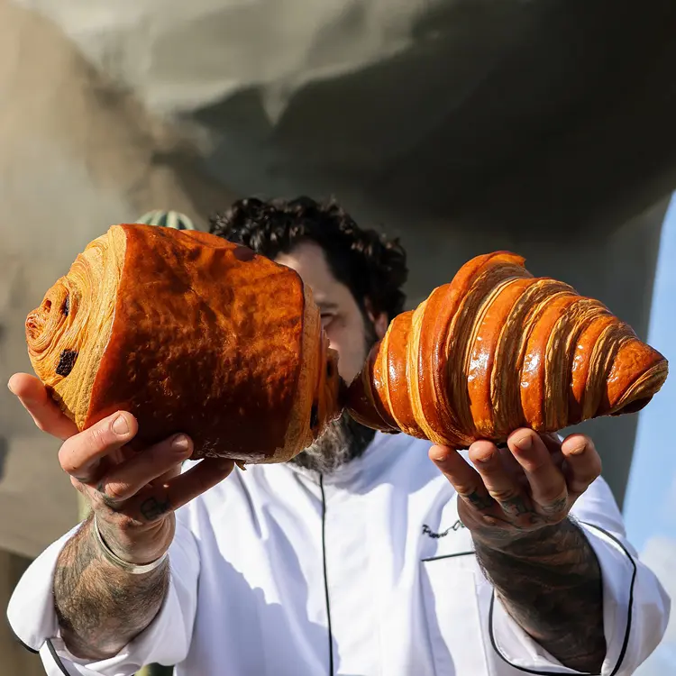 Notre boulanger qui porte le pain au chocolat XL et le croissant XL