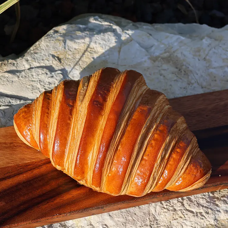 Zoom sur le croissant XL dans sur une planche en bois au soleil