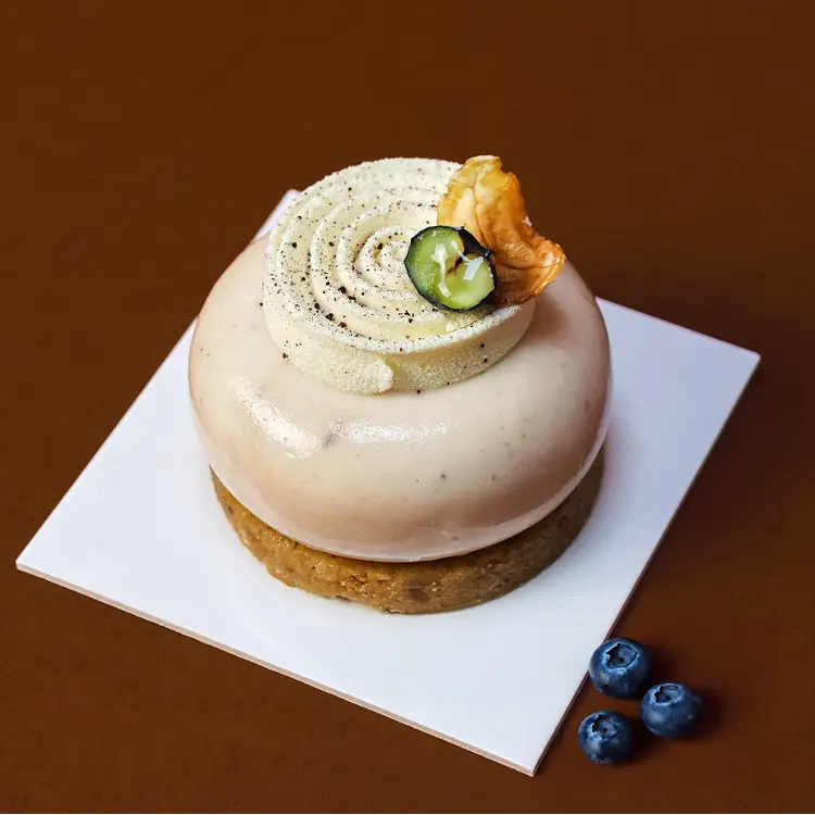 Zoom sur notre entremet marron et myrtille sur fond marron, avec des petites myrtilles posées à côté