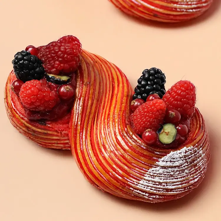 Notre viennoiserie en forme de signe "infini" pour la saint valentin, sur fond beige, où l'on voit les fruits rouges (framboises, mûres, myrtilles..)