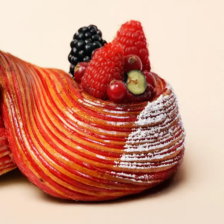 Zoom sur notre viennoiserie en forme de signe "infini" pour la saint valentin, sur fond beige, où l'on voit les fruits rouges (framboises, mûres, myrtilles..)