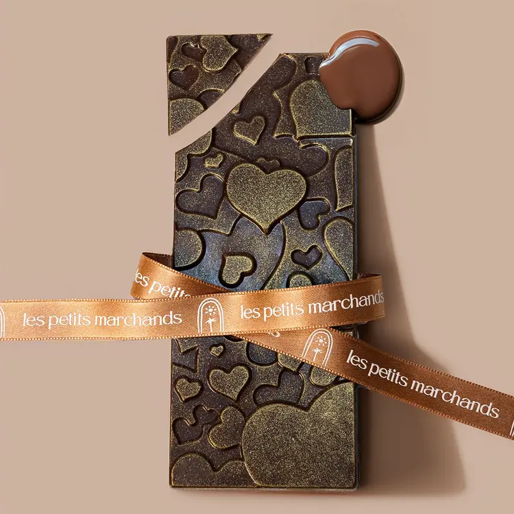 Zoom sur les motifs de notre tablette saint valentin au chocolat au lait, avec du chocolat coulant sur le côté, et un ruban Les Petits Marchands sur le dessus