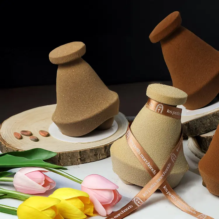 Mise en scène de notre collection de cloches en chocolat noir lait et blond, sur des rondins de bois avec des fleurs à côté