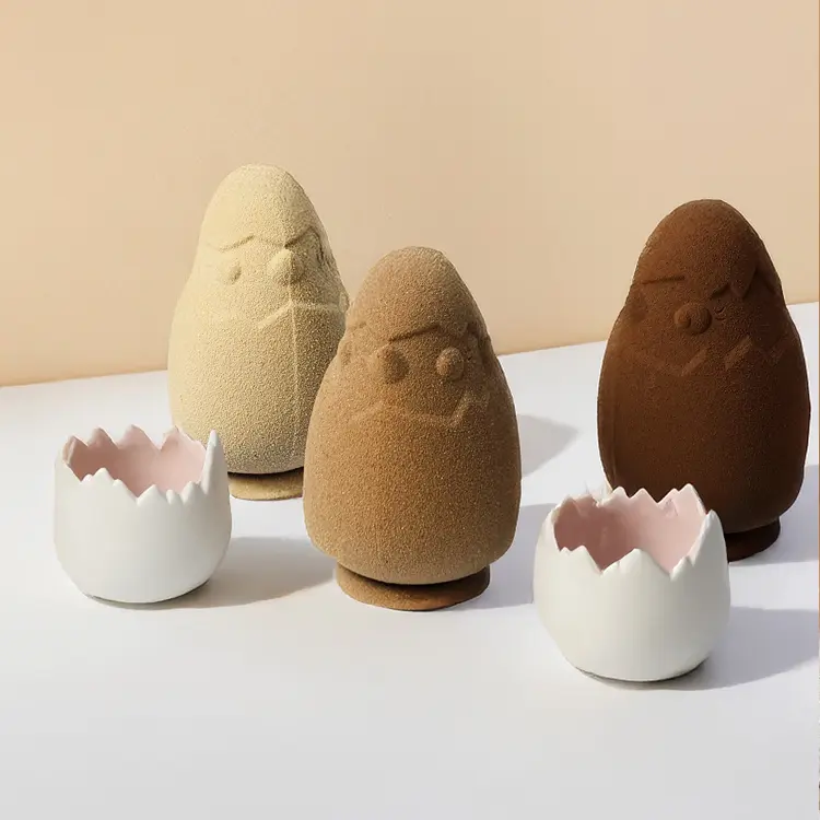 Trois poussins en chocolat noir lait et blond sur fond beige, avec des coquilles d'oeuf à côté