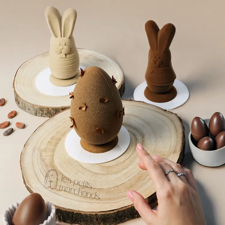 Mise en scène de Pâques avec une main qui s'apprête à prendre un petit oeuf praliné, autour des lapinou et lapinettes sur fond beige