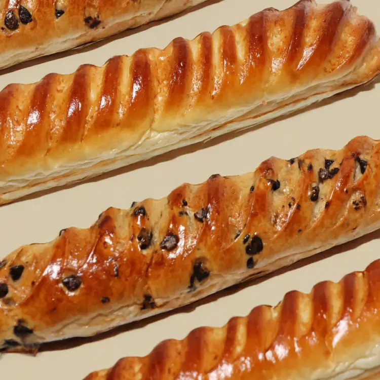 Plusieurs baguettes viennoises chocolat et nature posées sur un fond beige