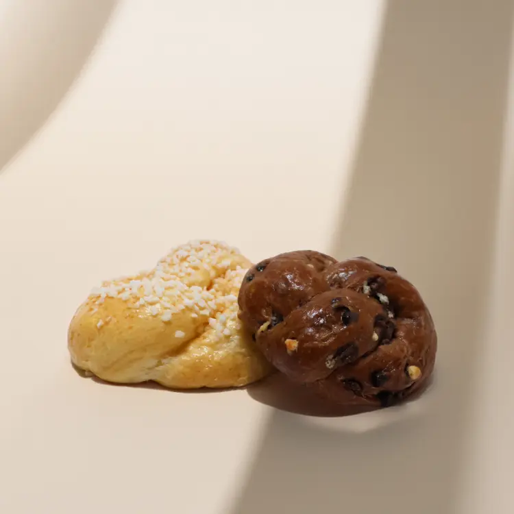 Deux brioches au sucre et tout chocolat posées sur fond beige avec des ombres autour