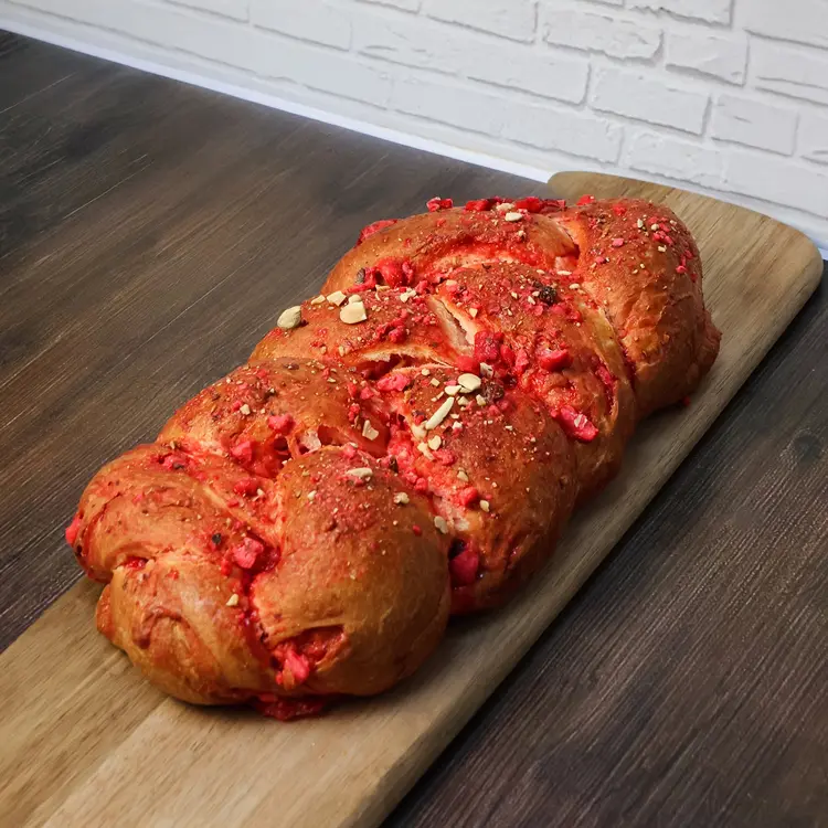 Brioche tressée 900g aux pralines roses posée sur une planche en bois dans un décor de cuisine