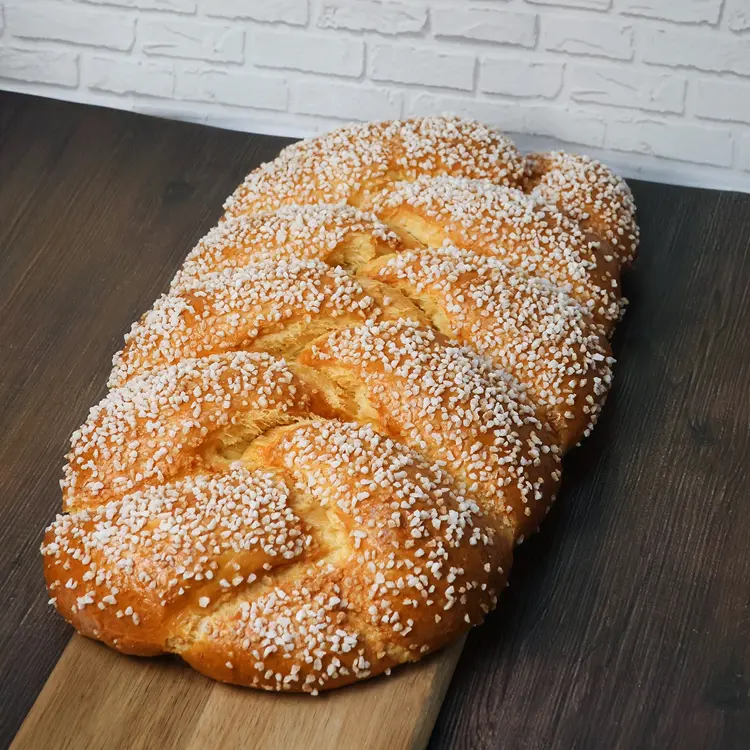 Brioche tressée au sucre et fleur d'oranger 900g posée sur une planche en bois dans un décor de cuisine