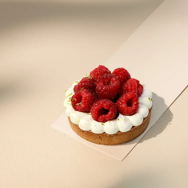 Tartelette framboise posée sur un fond beige avec quelques ombres autour