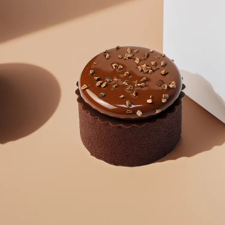 Notre entremet chocolat et gianduja sur fond beige avec quelques ombres autour