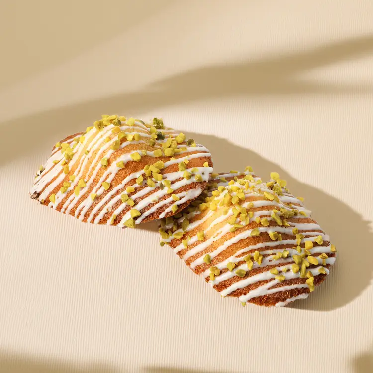 Deux madeleines pistaches l'une sur l'autre, sur fond beige avec quelques ombres autour