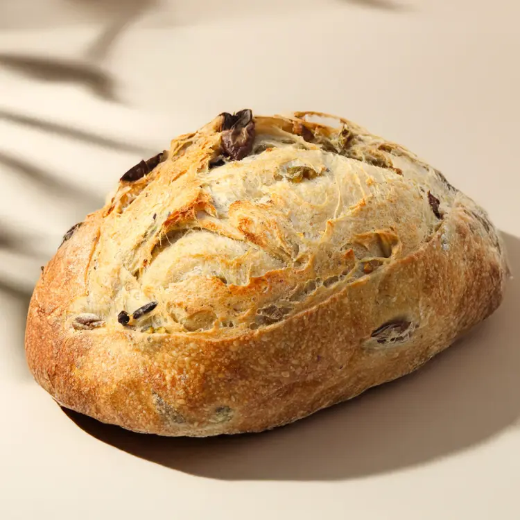 Pain aux olives sur fond beige avec quelques ombres autour avec des olives apparentes