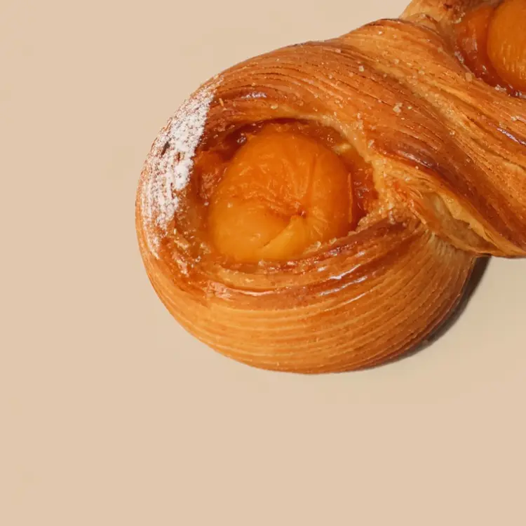 Zoom sur l'abricot de notre viennoiserie infini à l'abricot sur fond beige et sucre glace sur le dessus