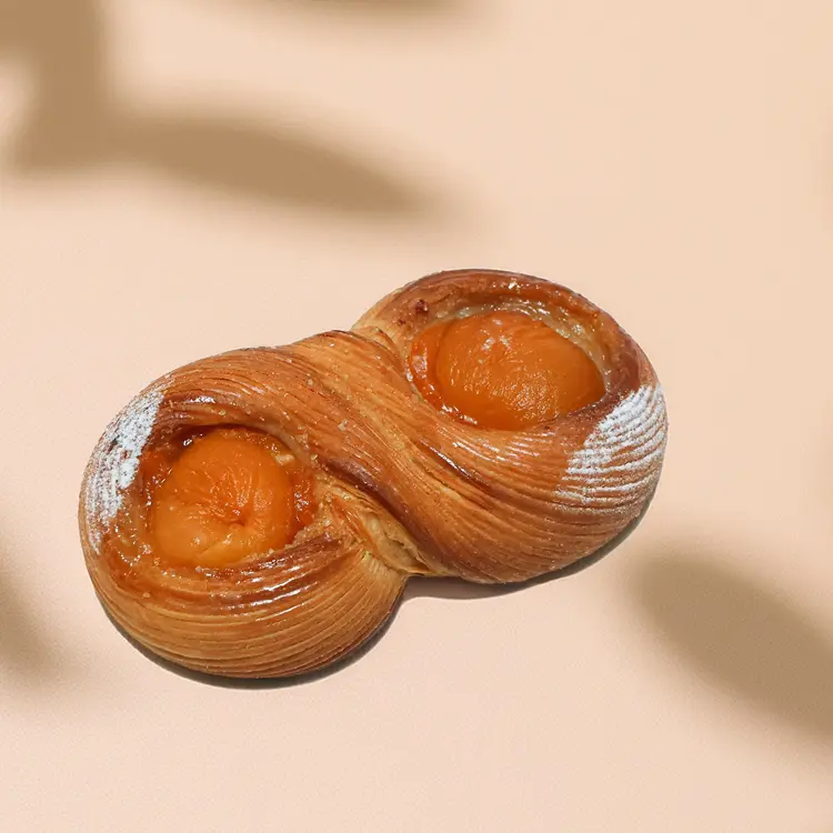 La viennoiserie infini à l'abricot sur fond beige avec quelques ombres et du sucre glace