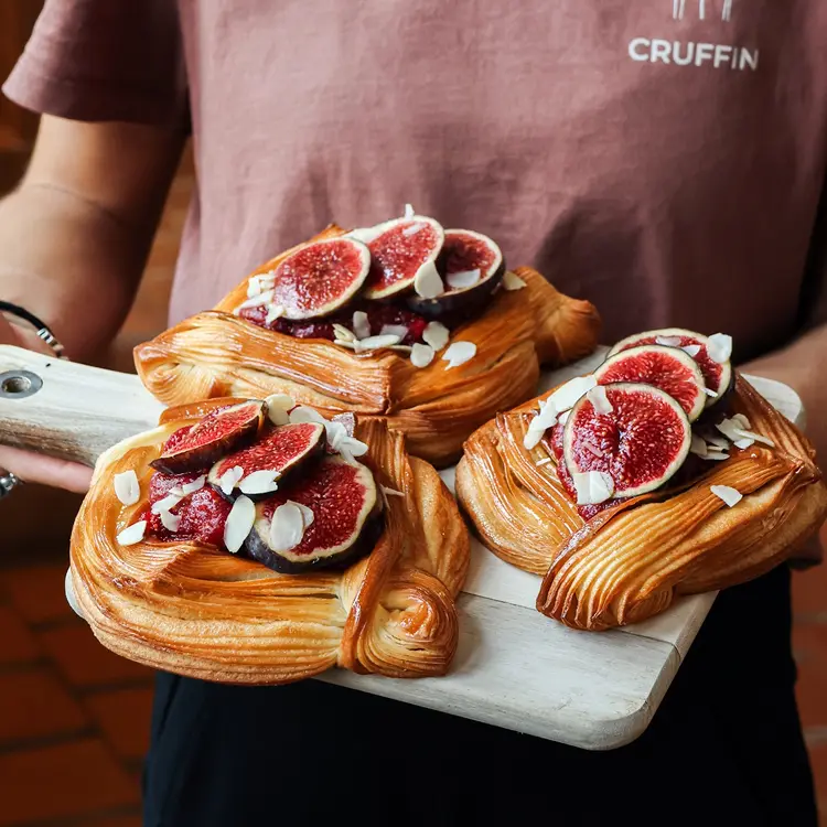 Notre responsable boutique qui porte une planche en bois avec trois viennoiseries panier de figue