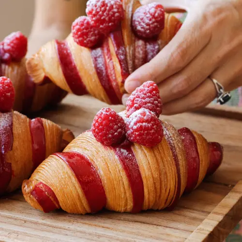 Plusieurs croissants bicolore à la framboise sur un plateau en bois, une main en porte l'un deux
