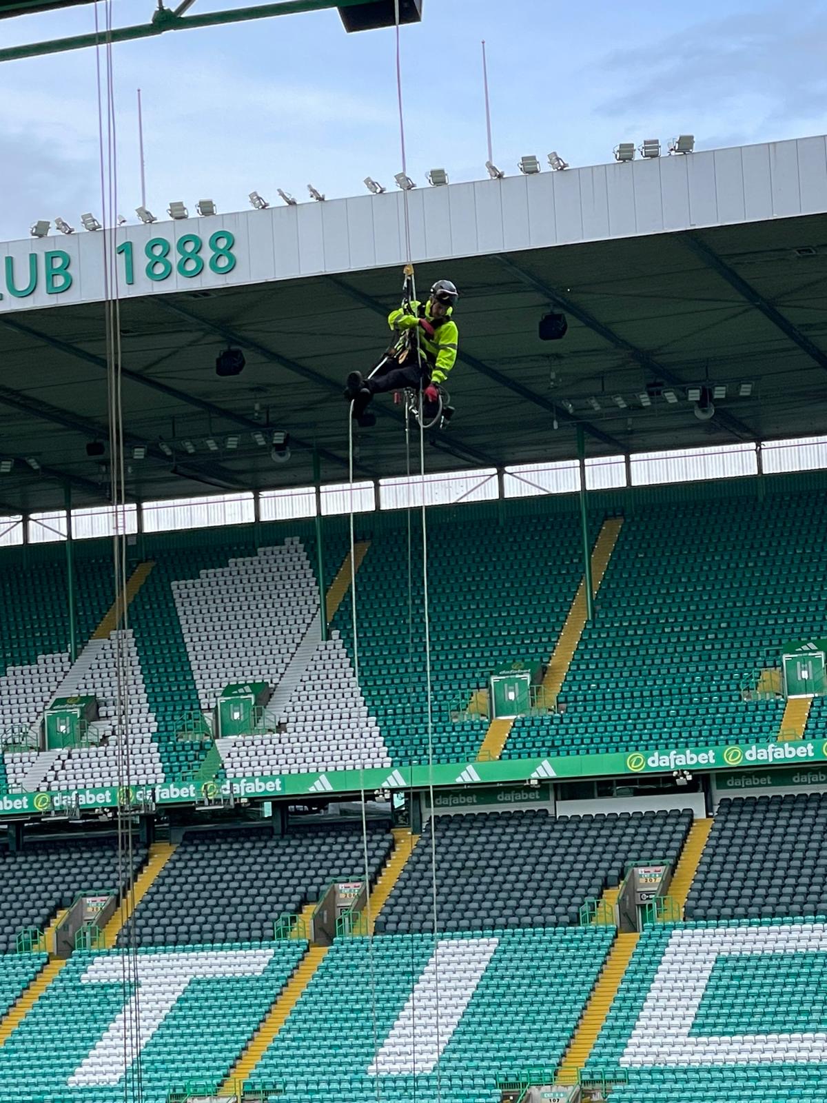 Roofing Advisors rope access operative abseiling inside Celtic Park stadium during segregation netting installation works