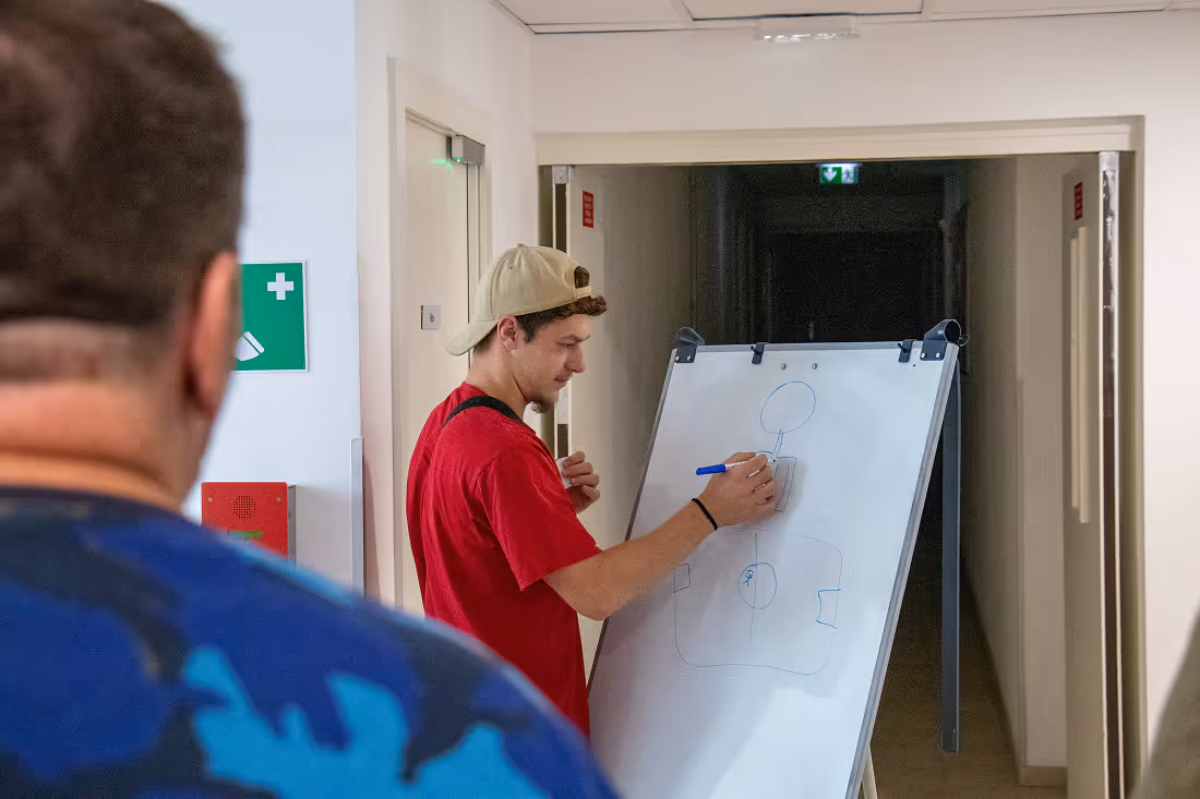 Trois jeunes adultes souriants dans une salle de bureau, deux tenant des ordinateurs portables Dell noirs, la femme au centre portant un pull beige.
