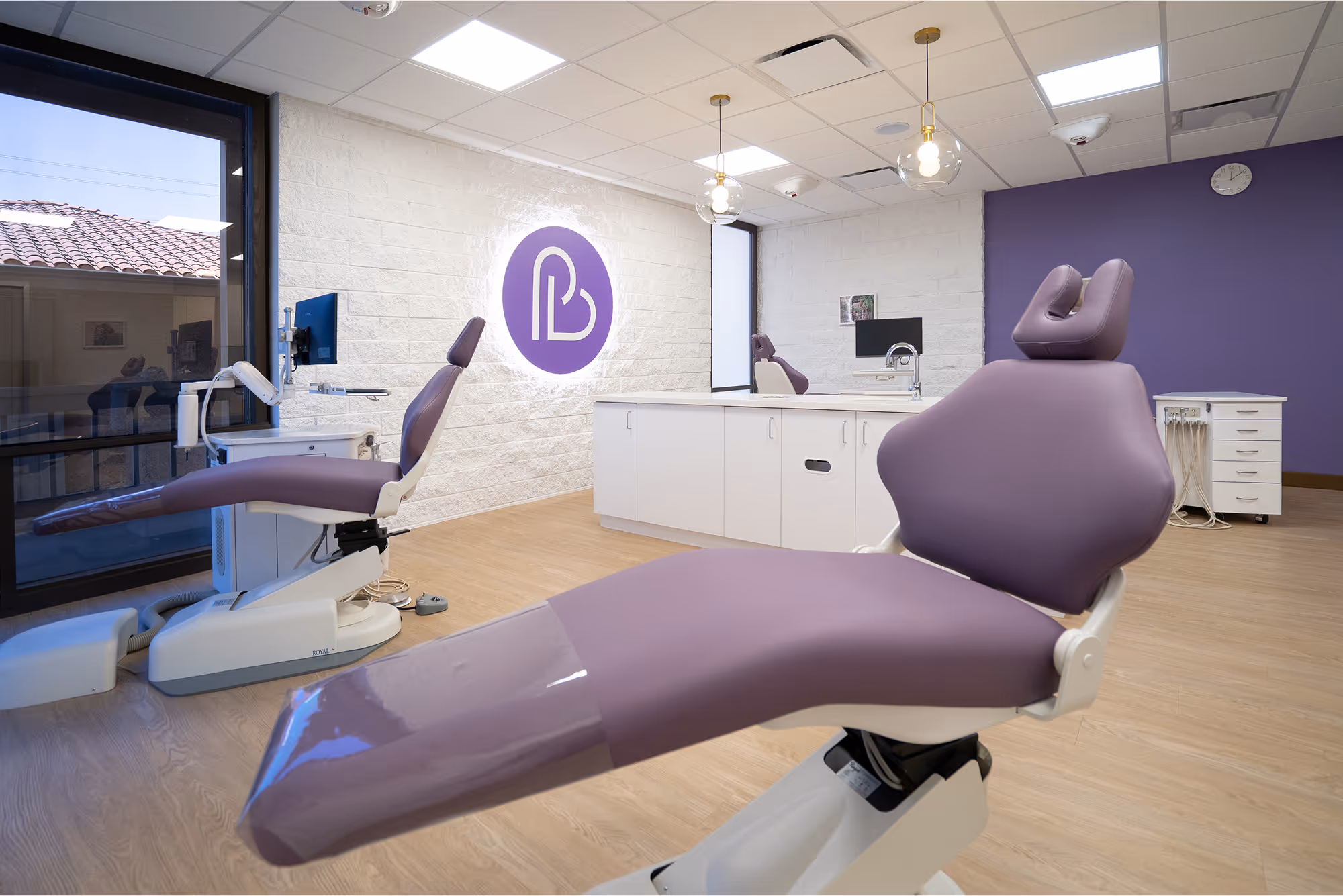 A dentist's office with a purple chair in front of a window.