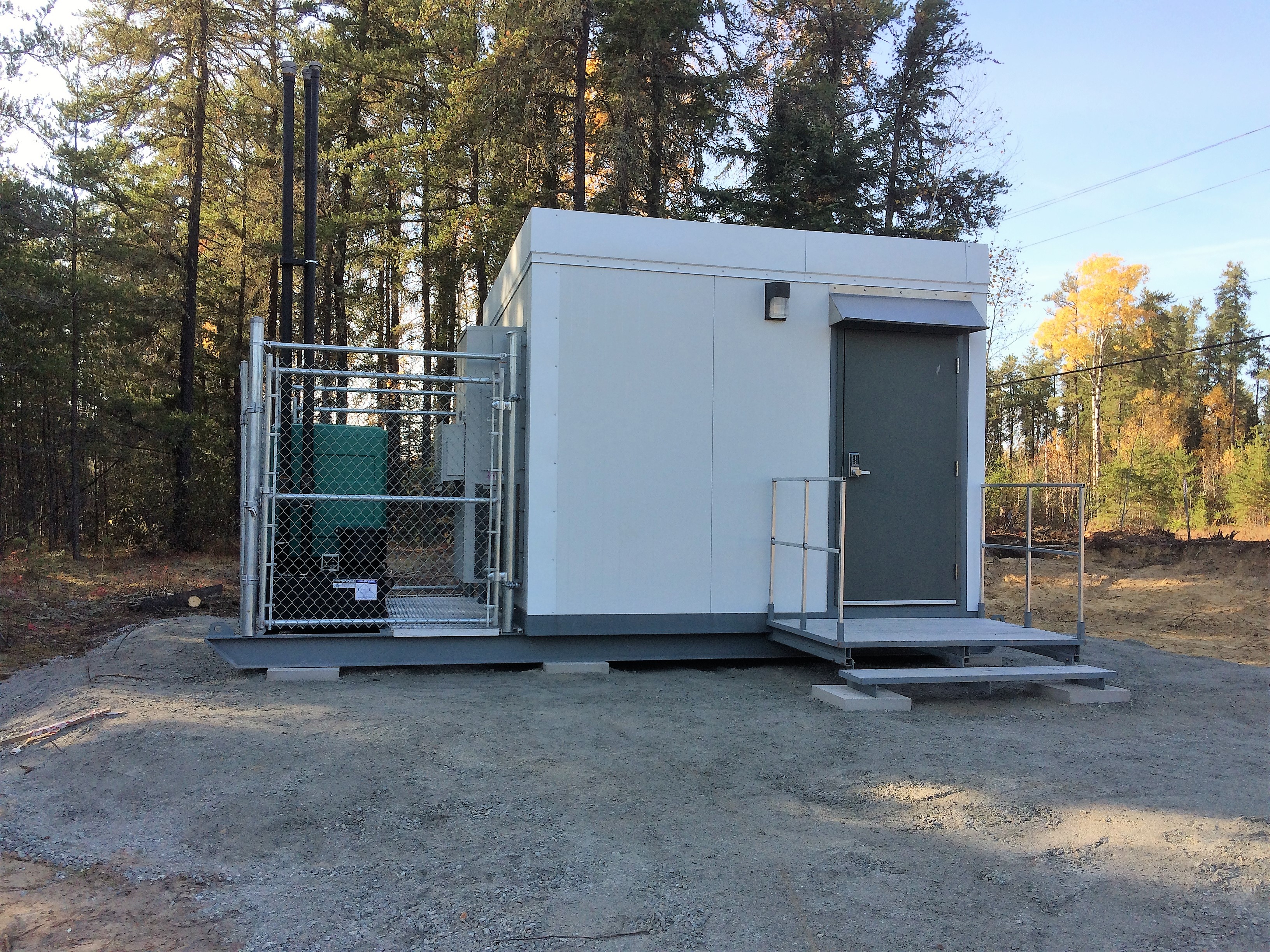 White container labeled Vortex Battery Energy Storage with solar panels and wind turbines nearby.