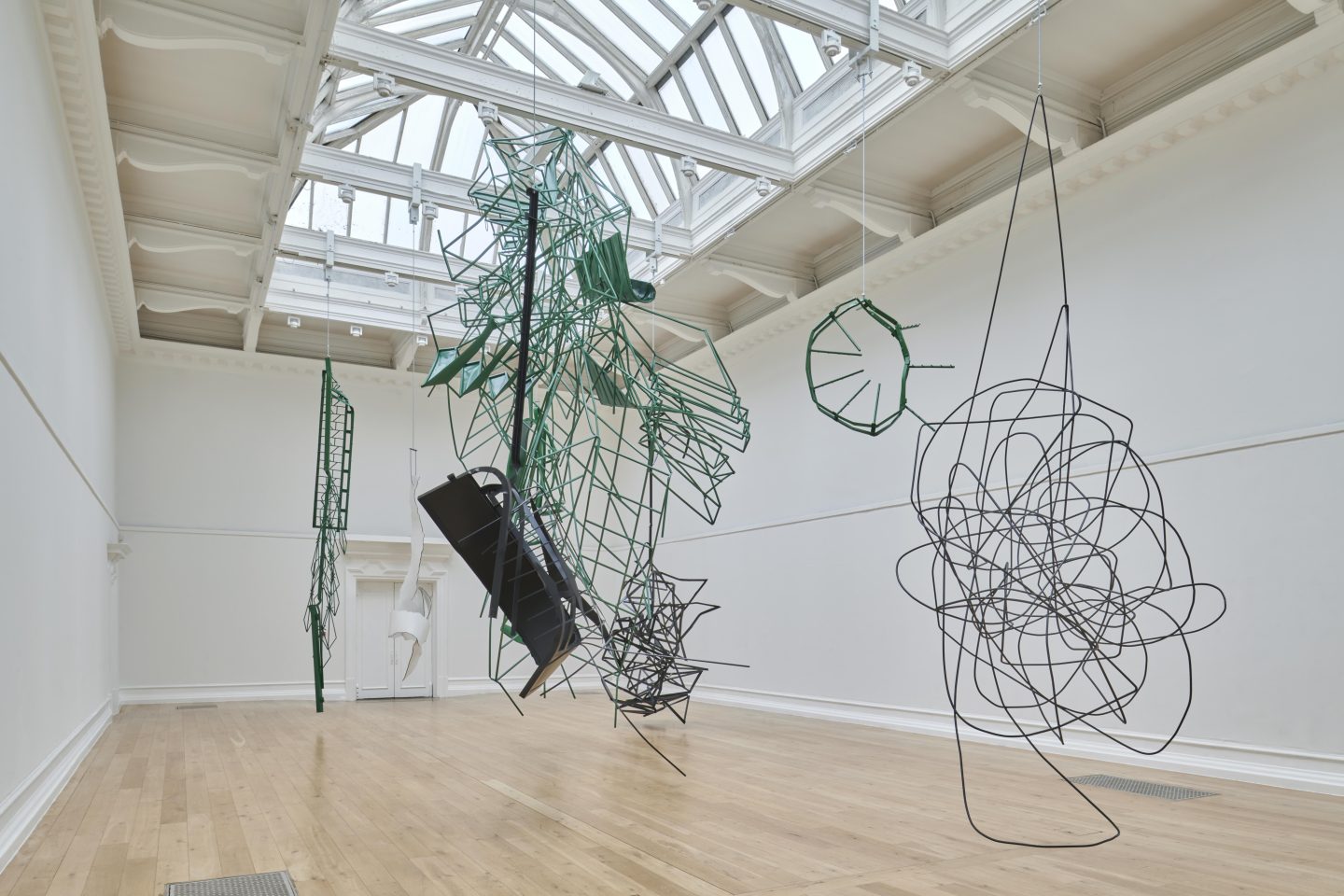 Large steel structures in black, white and green are suspended from a gallery ceiling