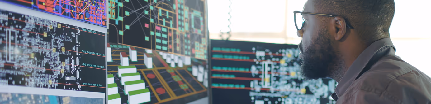 Engineer analyzing complex system schematics on multiple computer monitors, reviewing technical infrastructure and digital blueprints.