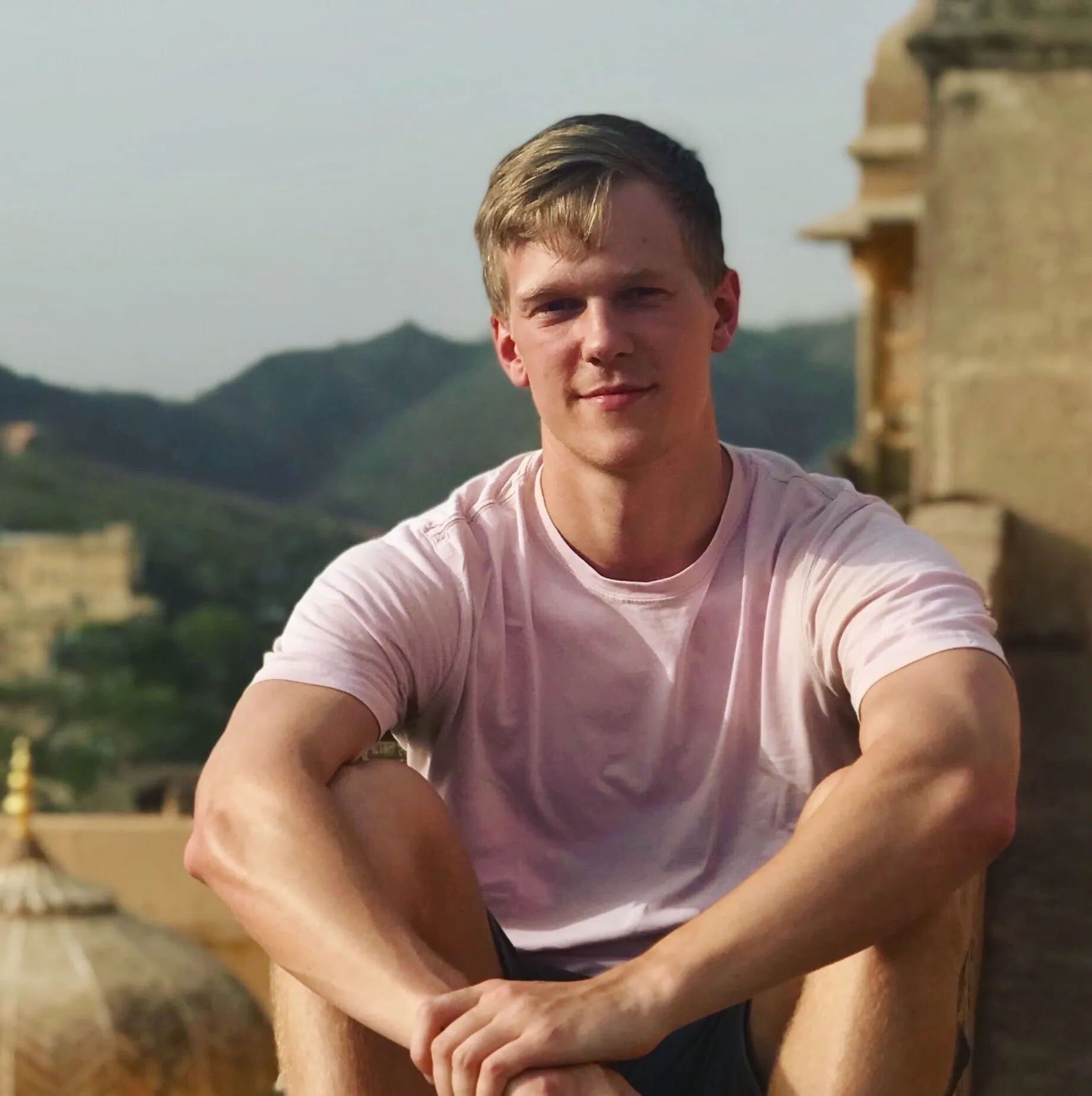 A man in a pink shirt sits on a wall.