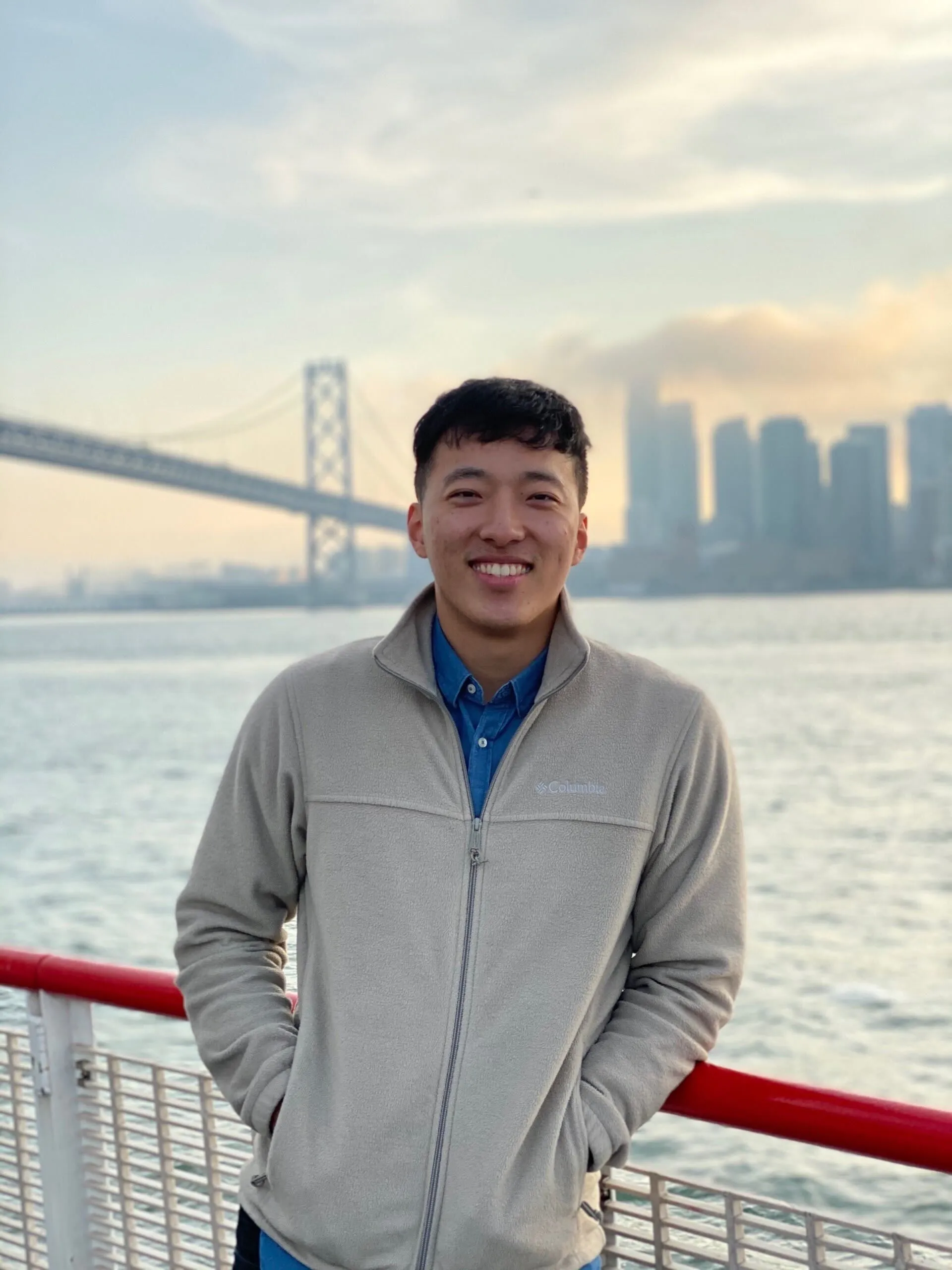 A man wearing a grey sweater and blue shirt standing on a boat.