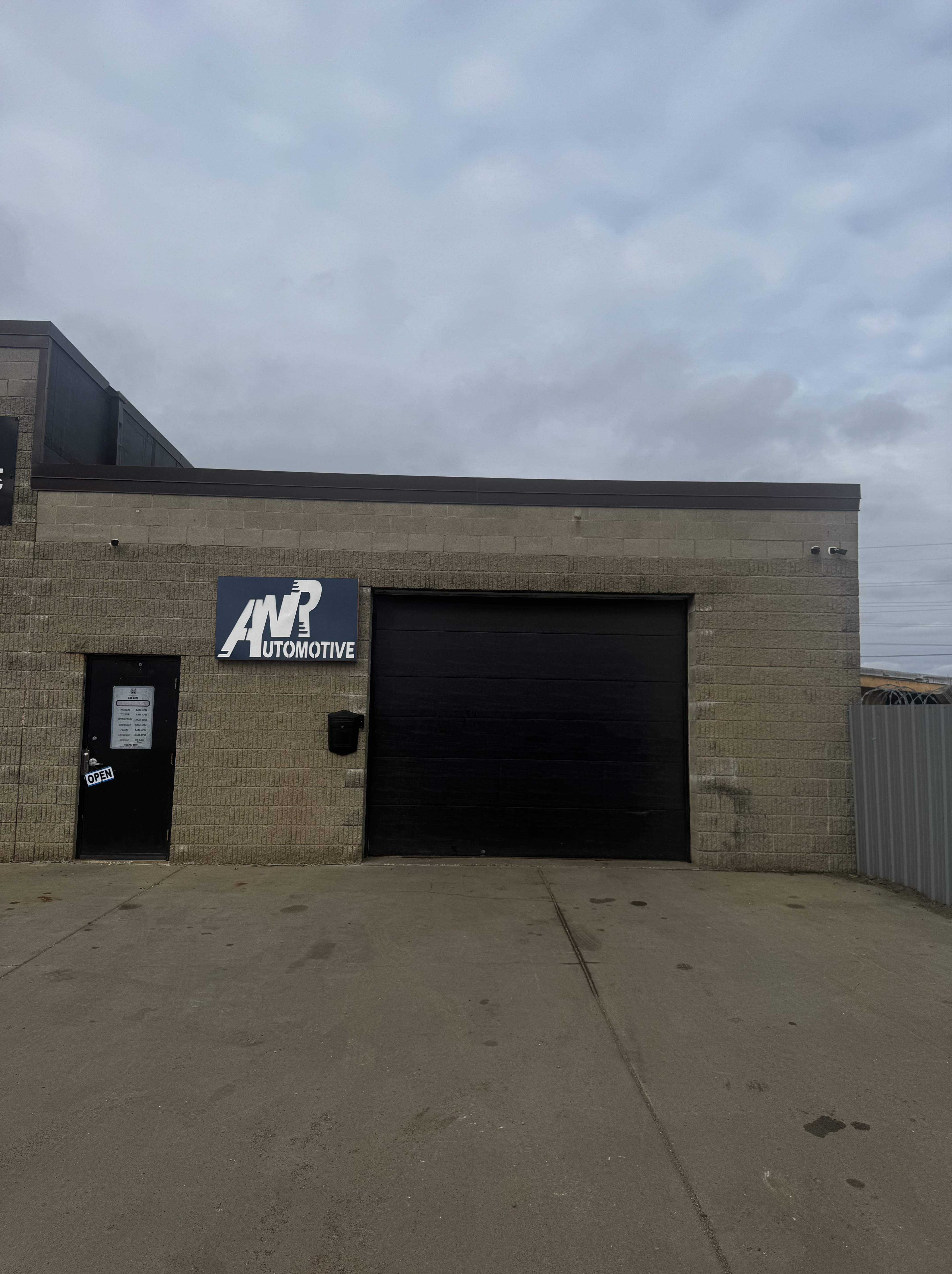 Front view of ANR Automotive shop building with the ANR Automotive sign above the entrance door and garage bay door in a commercial area.