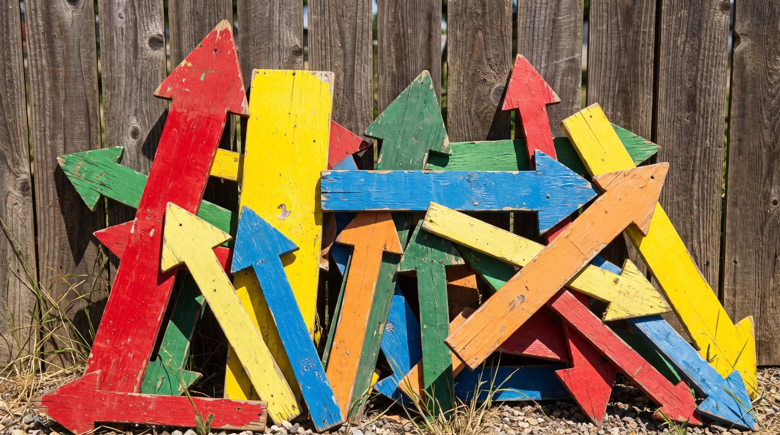 row of yard sign directional arrows leaning against a wooden fence