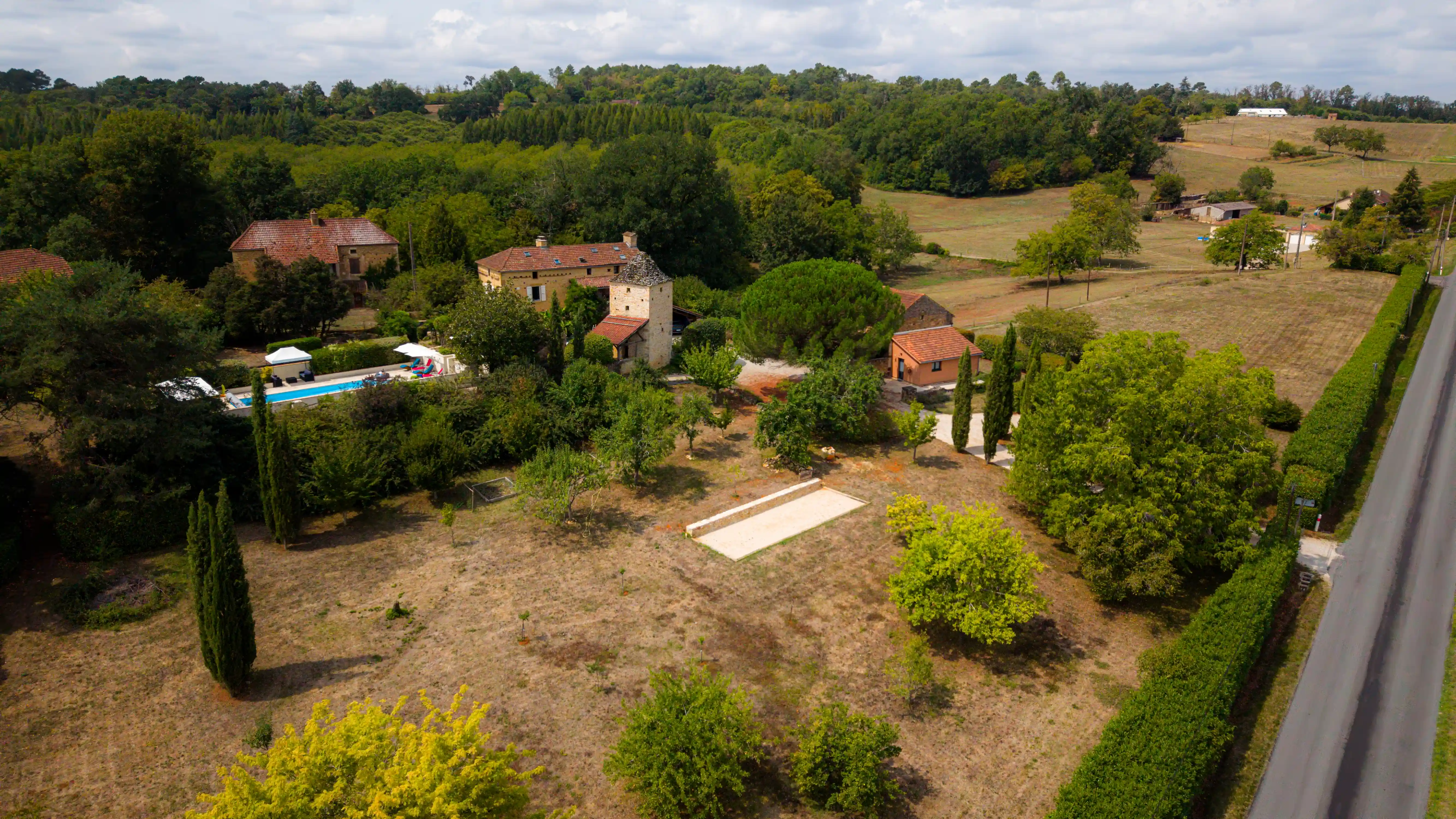 Photo drone prise de côté du Domaine du Pigeonnier avec : pigeonnier, piscine, verger, terrain de pétanque, parking et gîtes.