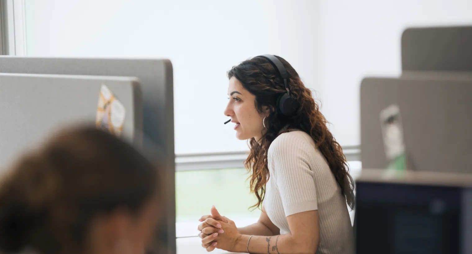 Eine Frau mit Headset sitzt in einem modernen Büro an einem Arbeitsplatz mit Sichtschutzwänden und spricht konzentriert in ein Mikrofon