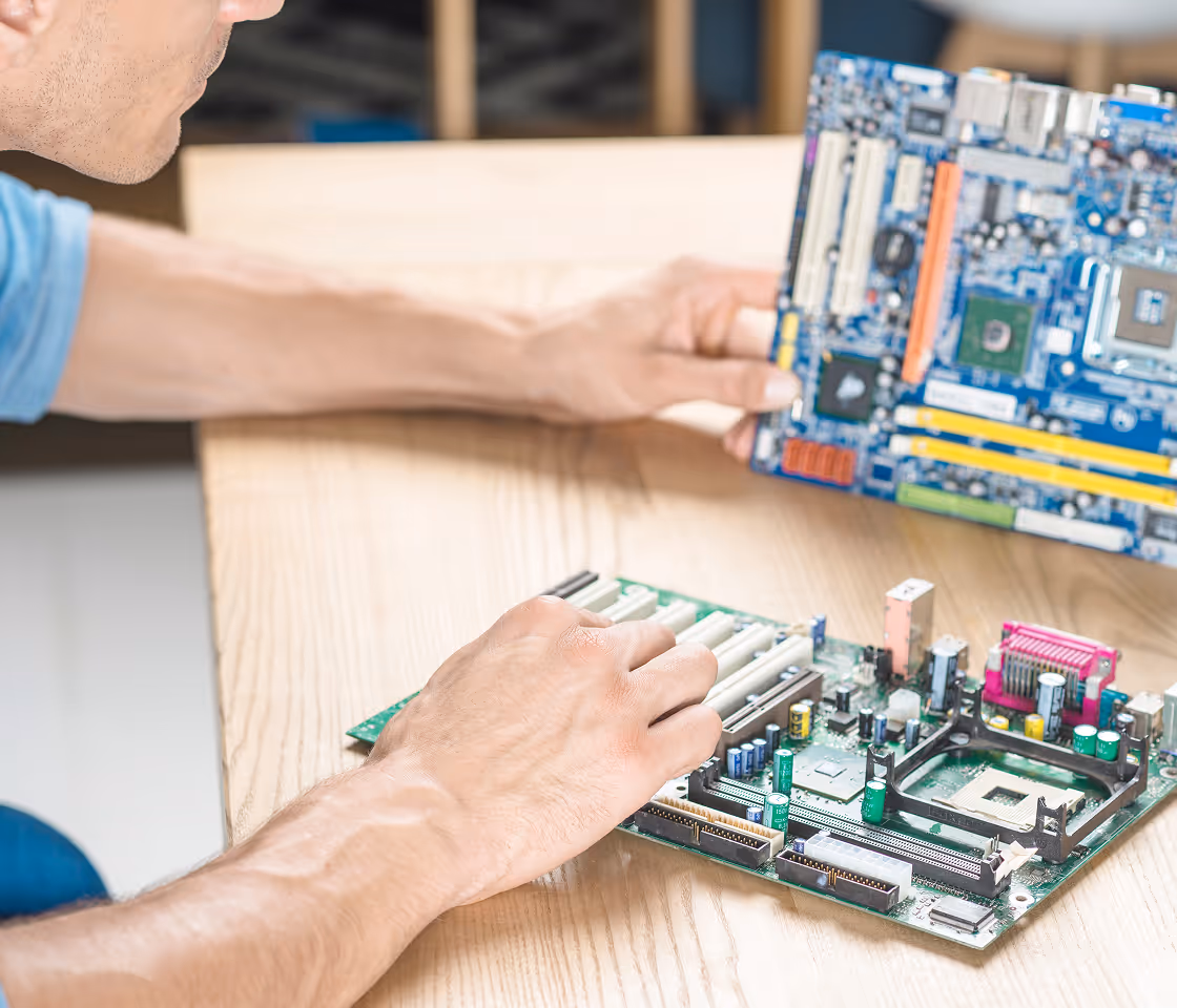 Person holding and examining two computer motherboards on a wooden table.