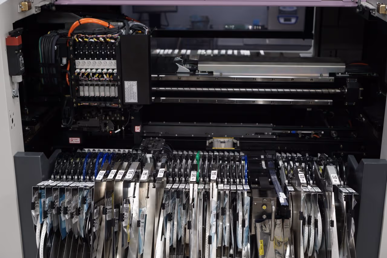 Close-up view of a PCB assembly machine with multiple reels of electronic components and wiring inside.