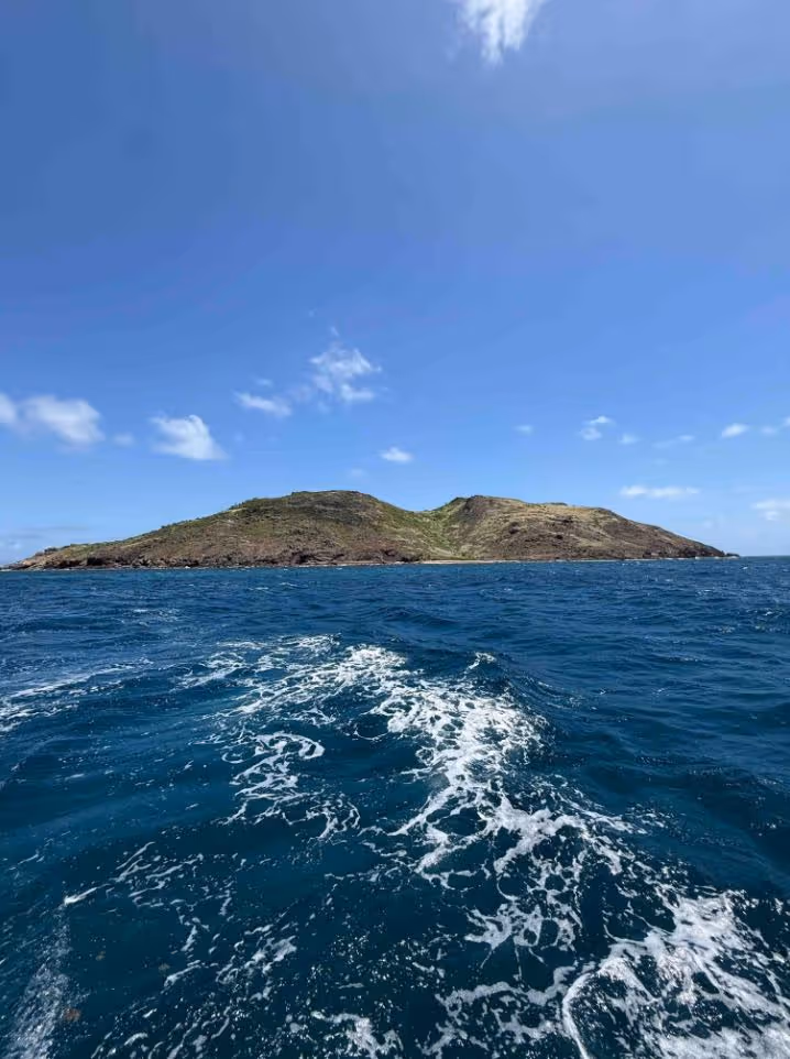 Formation rocheuse au bord d'une mer bleu profond sous un ciel bleu partiellement nuageux.