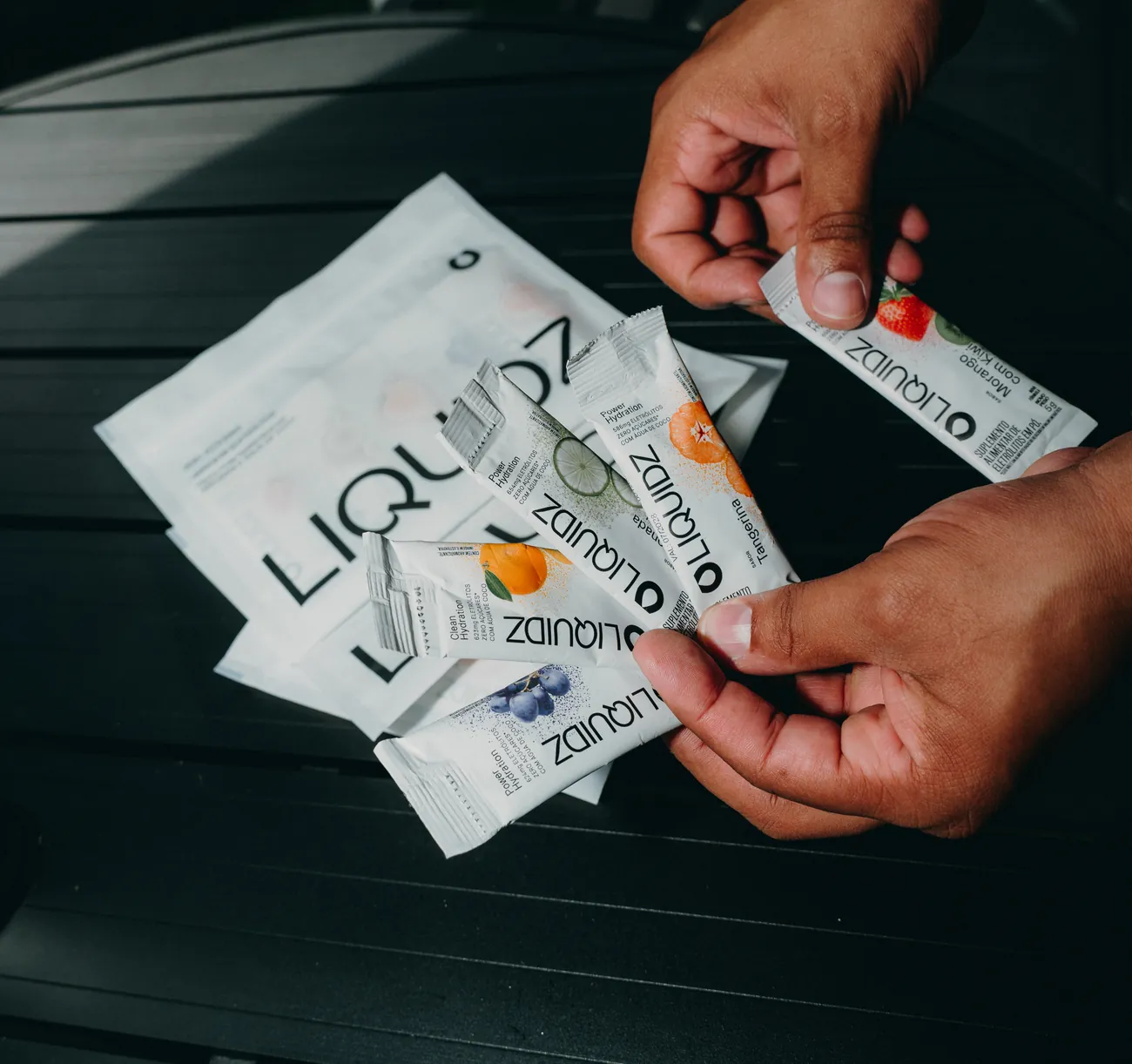 Mãos abrindo os sachês do kit degustação LIQUIDZ